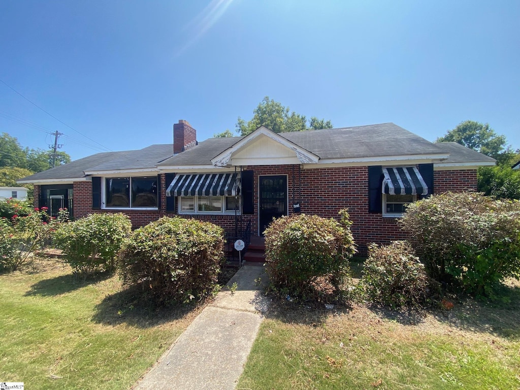 ranch-style house with brick siding, a chimney, and a front lawn