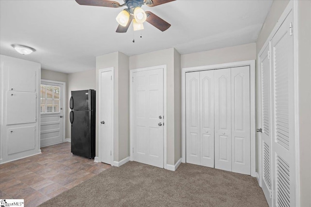 unfurnished bedroom featuring stone finish floor, baseboards, freestanding refrigerator, and a ceiling fan