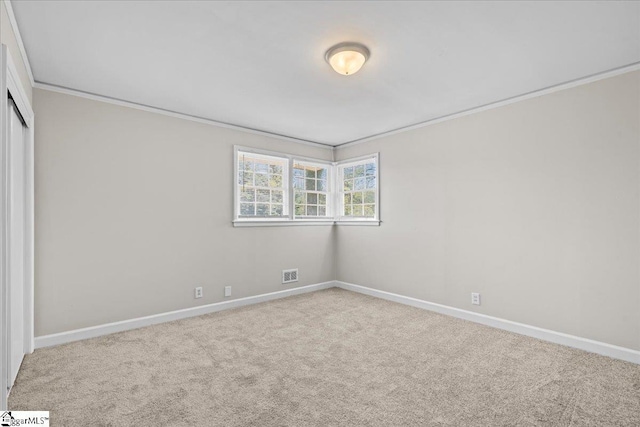 carpeted spare room featuring crown molding, visible vents, and baseboards