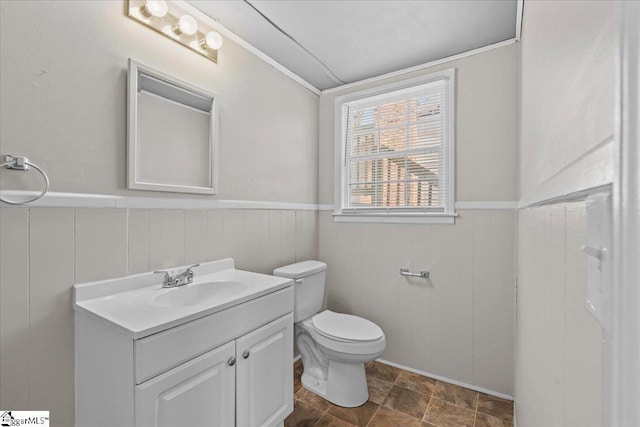 half bathroom featuring toilet, vanity, and a wainscoted wall