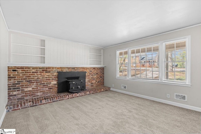unfurnished living room featuring a wood stove, carpet, visible vents, and baseboards