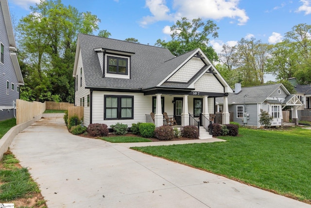 view of front of house featuring covered porch, fence, a front lawn, a shingled roof, and concrete driveway