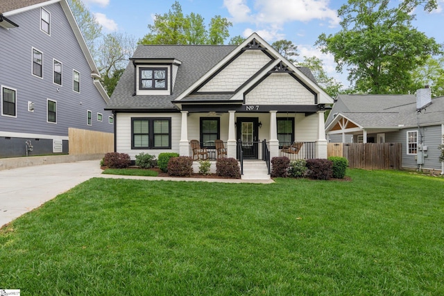 craftsman inspired home with a porch, roof with shingles, fence, and a front lawn