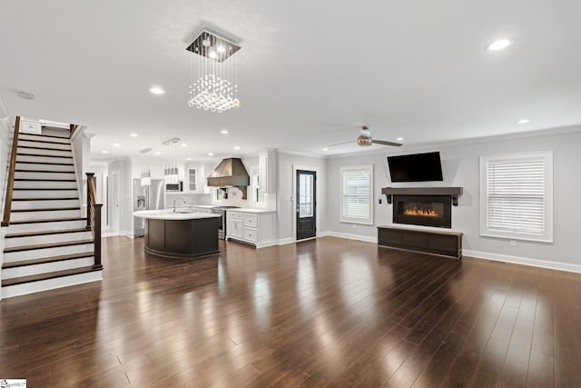 unfurnished living room featuring a glass covered fireplace, baseboards, ornamental molding, stairs, and ceiling fan with notable chandelier