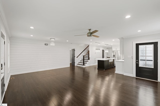 unfurnished living room featuring a sink, ornamental molding, ceiling fan, dark wood-style floors, and stairs
