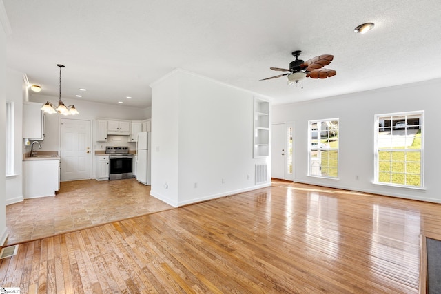 unfurnished living room featuring light wood-type flooring, ceiling fan with notable chandelier, a sink, and visible vents