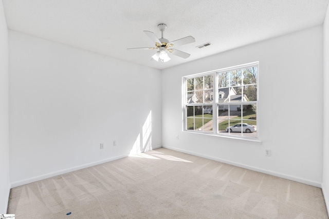 carpeted spare room with visible vents, baseboards, and a ceiling fan