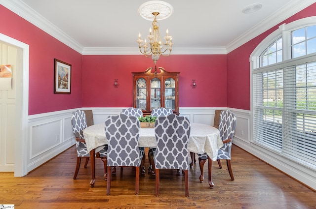 dining area with crown molding, wood finished floors, an inviting chandelier, and wainscoting