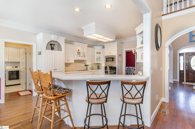 kitchen with a kitchen bar, arched walkways, light wood-style flooring, stainless steel microwave, and washer / dryer