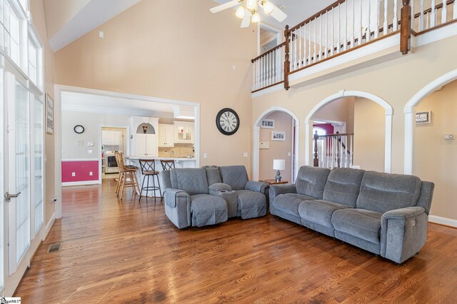 living room with visible vents, arched walkways, a high ceiling, a ceiling fan, and wood finished floors