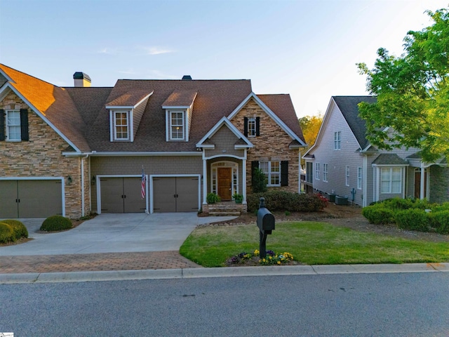 view of front facade with a front yard, stone siding, an attached garage, a chimney, and concrete driveway