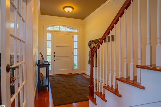 foyer with wood finished floors, ornamental molding, and stairway