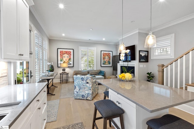 kitchen featuring light wood-style floors, light stone countertops, a kitchen bar, ornamental molding, and white cabinets