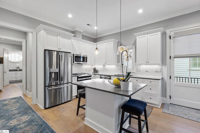 kitchen featuring pendant lighting, a kitchen bar, white cabinetry, appliances with stainless steel finishes, and backsplash