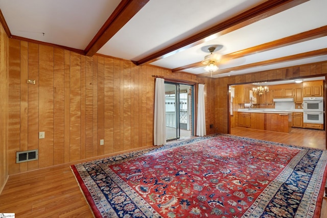 living room with light wood-type flooring, a ceiling fan, wood walls, visible vents, and beam ceiling