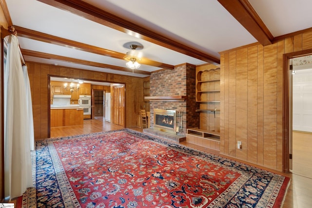 unfurnished living room with beamed ceiling, a brick fireplace, and wood walls