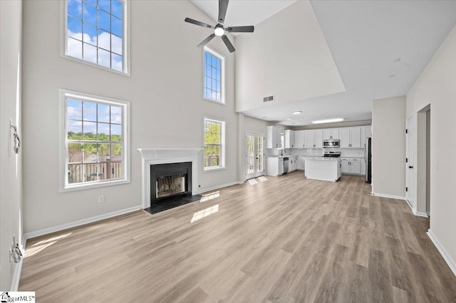 unfurnished living room featuring a fireplace with raised hearth, visible vents, baseboards, and ceiling fan