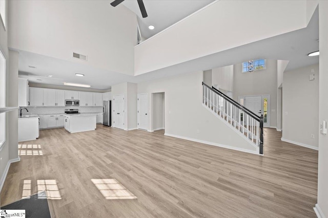 unfurnished living room featuring visible vents, a ceiling fan, a towering ceiling, and stairs