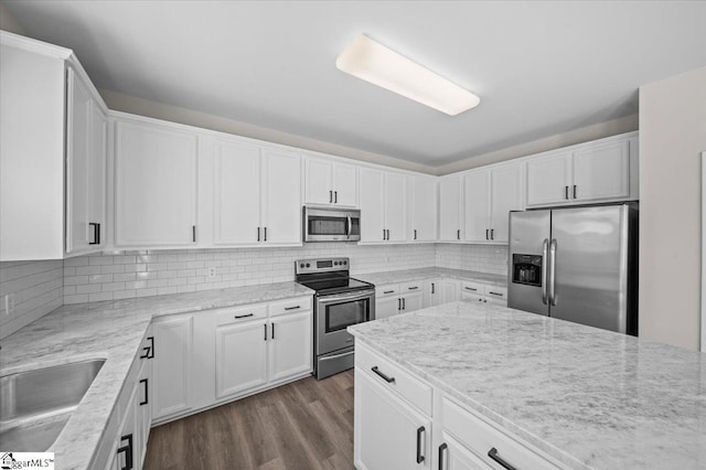 kitchen featuring tasteful backsplash, white cabinets, dark wood-type flooring, appliances with stainless steel finishes, and a sink