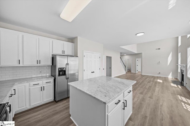 kitchen featuring stainless steel fridge with ice dispenser, backsplash, light wood-style flooring, and a kitchen island