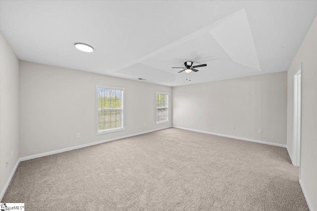 spare room featuring a tray ceiling, baseboards, a ceiling fan, and carpet