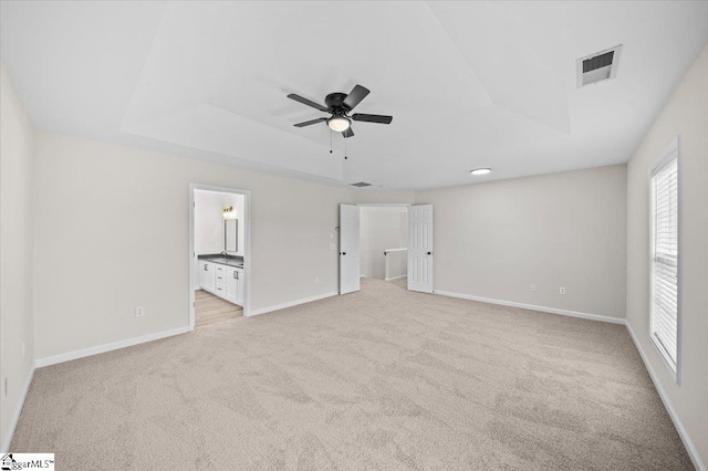 unfurnished bedroom featuring visible vents, baseboards, a raised ceiling, ensuite bathroom, and light carpet