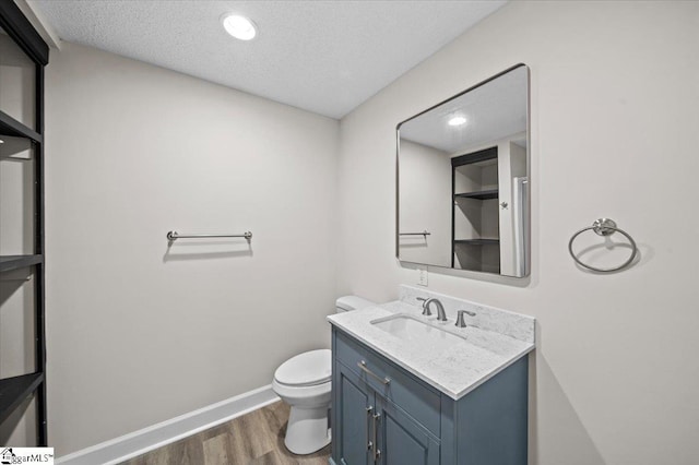 bathroom with a textured ceiling, vanity, toilet, wood finished floors, and baseboards