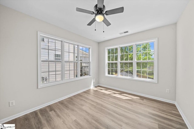 empty room featuring wood finished floors, baseboards, a ceiling fan, and visible vents