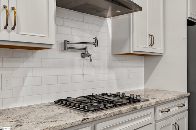 kitchen featuring light stone counters, white cabinetry, backsplash, stainless steel gas stovetop, and ventilation hood