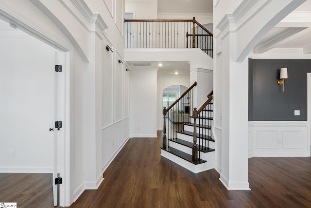 staircase featuring arched walkways, a high ceiling, and wood finished floors