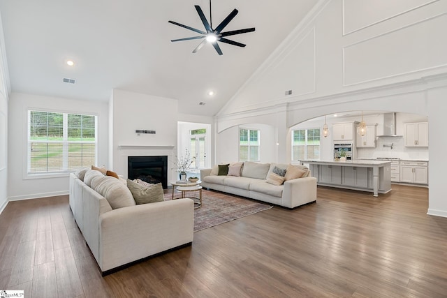 living area featuring high vaulted ceiling, ceiling fan, a glass covered fireplace, visible vents, and plenty of natural light