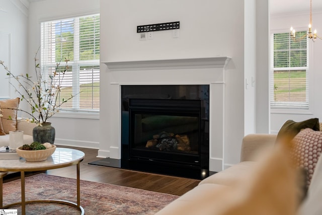 living area featuring a chandelier, wood finished floors, a glass covered fireplace, and a wealth of natural light