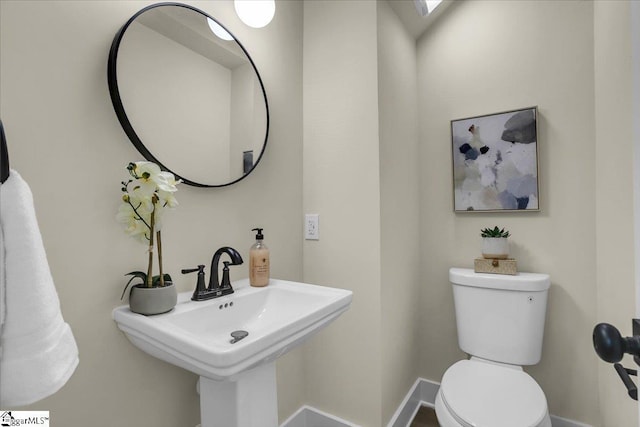 half bathroom with toilet, a sink, and baseboards