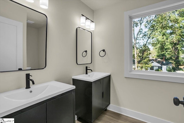 bathroom featuring a sink, baseboards, two vanities, and wood finished floors