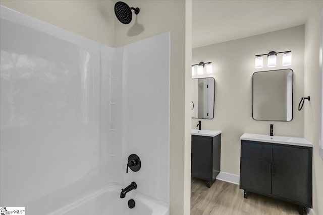 full bath with two vanities, washtub / shower combination, a sink, and wood finished floors
