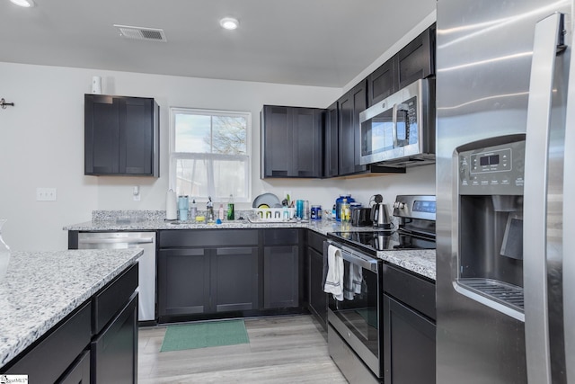 kitchen featuring light wood-style flooring, visible vents, light stone counters, and appliances with stainless steel finishes