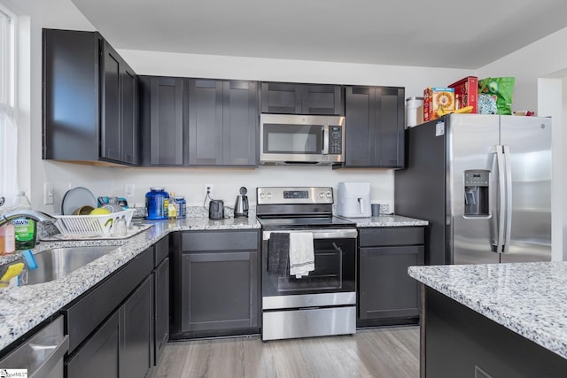 kitchen featuring a sink, light wood-style flooring, light stone counters, and stainless steel appliances