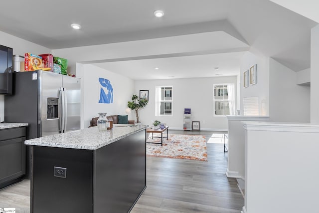 kitchen with light wood-type flooring, light stone counters, stainless steel fridge, open floor plan, and a center island