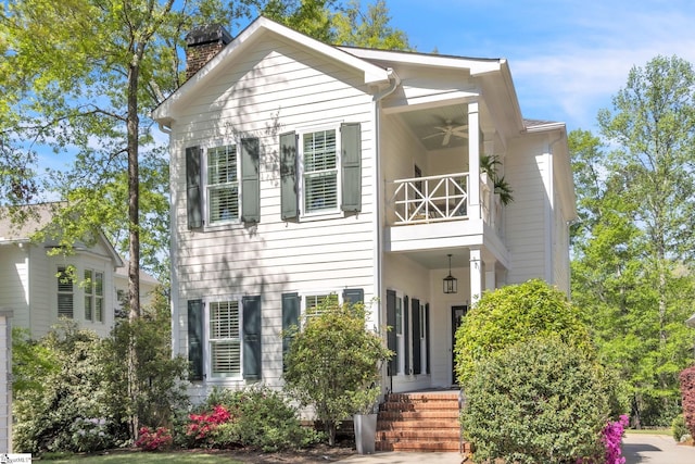 view of front of home with a balcony, a chimney, and ceiling fan