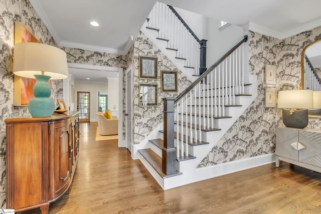staircase with crown molding, baseboards, wood finished floors, and wallpapered walls