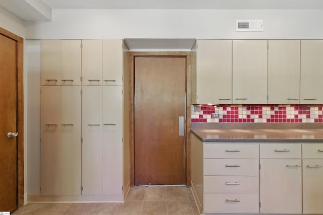 kitchen with light tile patterned floors, visible vents, cream cabinetry, and decorative backsplash