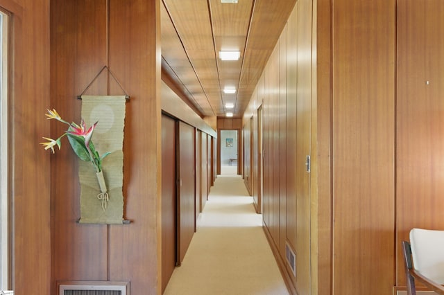 hallway featuring visible vents, light colored carpet, and wood walls