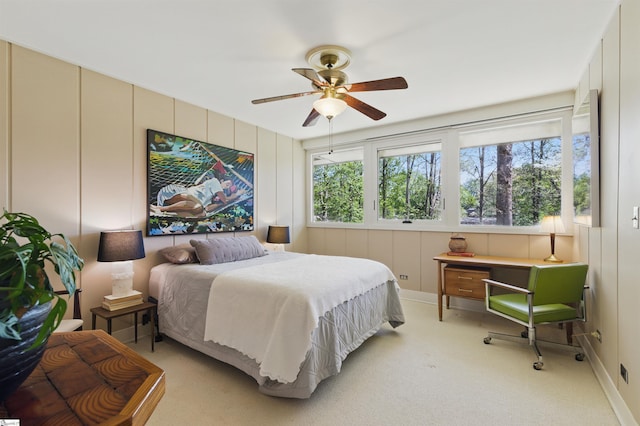 bedroom with a decorative wall, light colored carpet, and ceiling fan