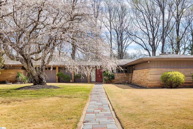 mid-century inspired home featuring stone siding, fence, and a front lawn