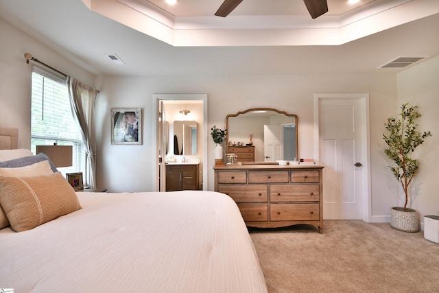 bedroom featuring light carpet, visible vents, a tray ceiling, and ensuite bathroom
