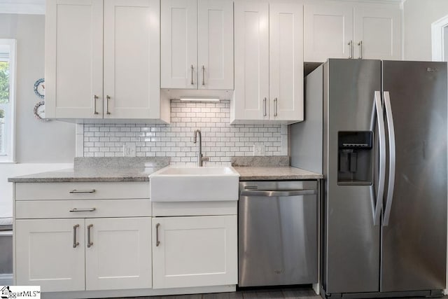 kitchen featuring white cabinets, a sink, appliances with stainless steel finishes, light stone countertops, and decorative backsplash