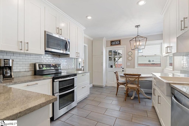 kitchen with tasteful backsplash, ornamental molding, white cabinetry, a chandelier, and appliances with stainless steel finishes