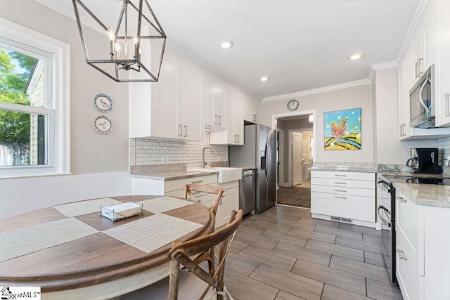 kitchen with a notable chandelier, white cabinets, decorative backsplash, stainless steel appliances, and a sink