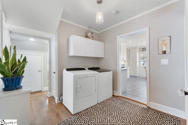 washroom featuring baseboards, ornamental molding, light wood-style floors, cabinet space, and washing machine and clothes dryer