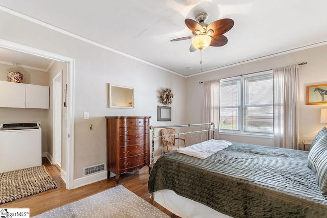 bedroom featuring ornamental molding, visible vents, wood finished floors, washer / dryer, and baseboards